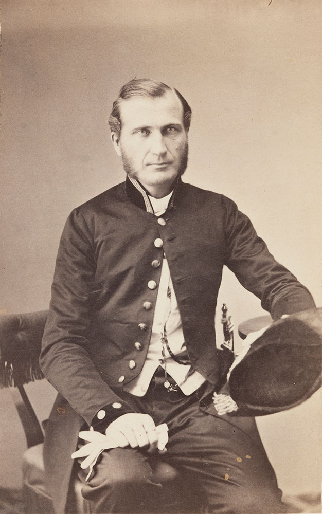 Nimismiehen virkapukuun 1800-luvun loppupuolella kuului tumma sortuutti ja juhlakäytössä kaksikolkkahattu ja virkamiekka.  Arkisin käytettiin tummanvihreää virkalakkia. Sauvon nimismies Carl Johan Sevonius. Kuva: Museovirasto.